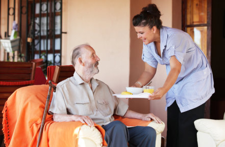 a female caregiver serving an elderly man